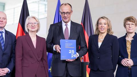 Prof. Dr. Monika Schnitzer, Friedrich Merz und Mitglieder des Sachverständigenrates stehen dicht nebeneinander bei der Übergabe des Jahresgutachtens 2025/2026.