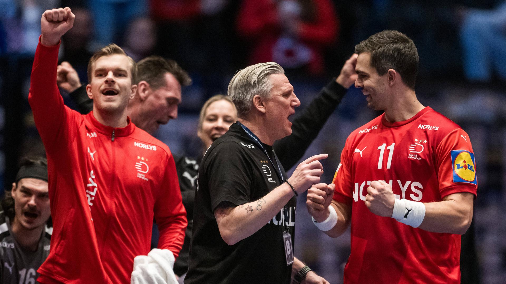 Dänemarks Trainer Nikolaj Jacobsen in der Mitte im schwarzen T-Shirt und zwei seiner Spieler in roten Trikots jubeln und gestikulieren.