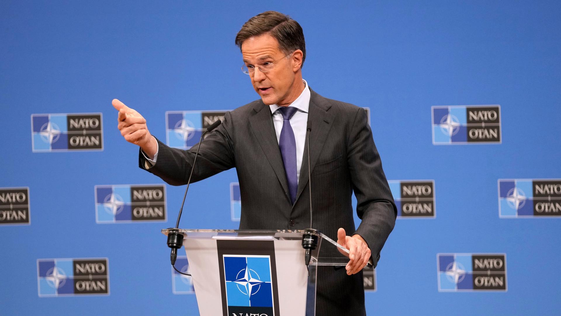  Mark Rutte spricht an einem Redepult, im Hintergrund sind NATO-Logos auf einer blauen Wand zu sehen.