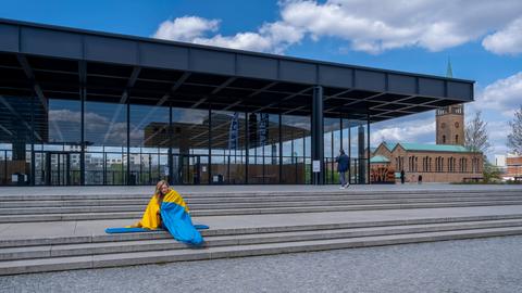 Eine Frau eingehüllt in die ukrainische Flagge vor der Neuen Nationalgalerie in Berlin.