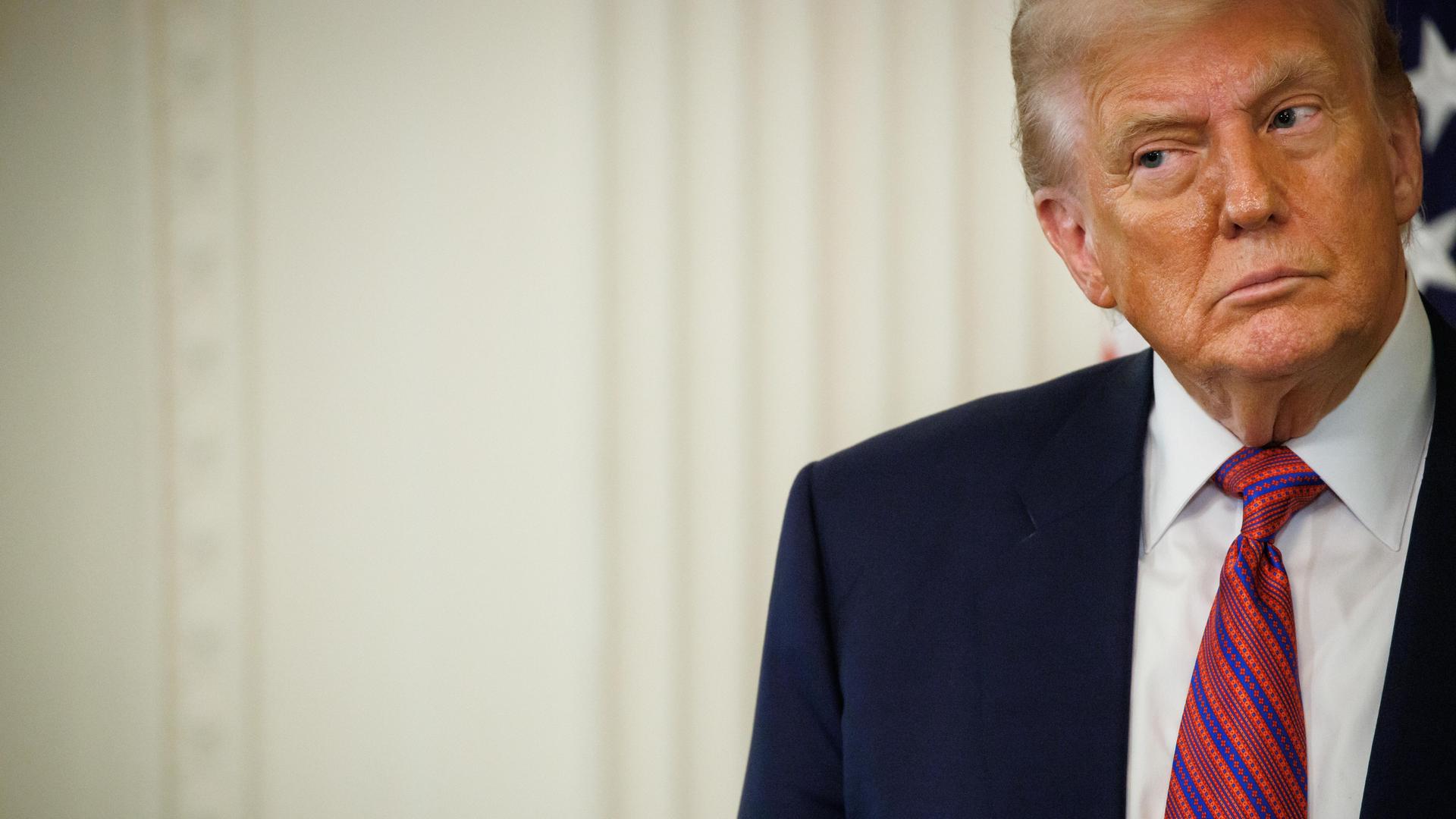 US-Präsident Donald Trump in Anzug und mit Krawatte vor einem hellen Hintergrund schaut skeptisch zur Seite US-Präsident Donald Trump in Anzug und mit Krawatte vor einem hellen Hintergrund schaut skeptisch zur Seite