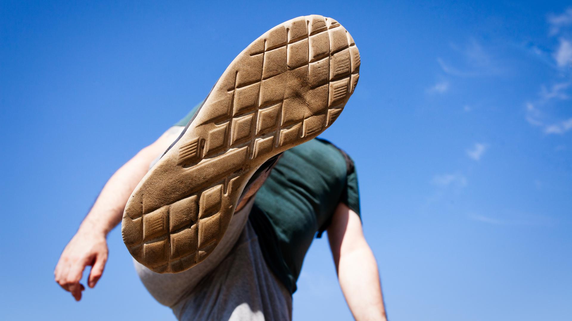 Eine Ansicht von unten wie ein junger Mensch seinen Fuß hoch in die Luft hebt, um jemanden oder etwas zu treten oder zu zertreten.