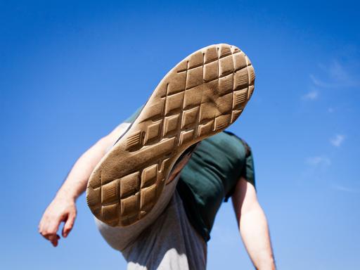 Eine Ansicht von unten wie ein junger Mensch seinen Fuß hoch in die Luft hebt, um jemanden oder etwas zu treten oder zu zertreten. Eine Ansicht von unten wie ein junger Mensch seinen Fuß hoch in die Luft hebt, um jemanden oder etwas zu treten oder zu zertreten.