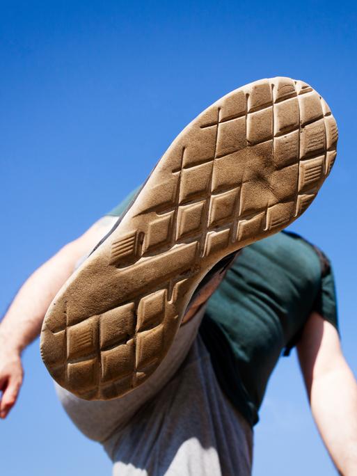 Eine Ansicht von unten wie ein junger Mensch seinen Fuß hoch in die Luft hebt, um jemanden oder etwas zu treten oder zu zertreten. Eine Ansicht von unten wie ein junger Mensch seinen Fuß hoch in die Luft hebt, um jemanden oder etwas zu treten oder zu zertreten.