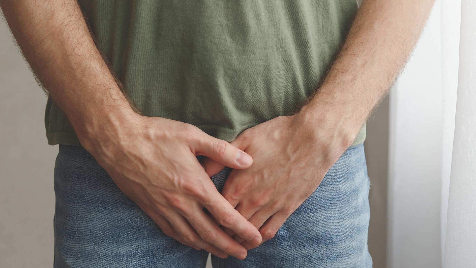 Ein Mann in Jeans hält die Hände vor seine Leistengegend.