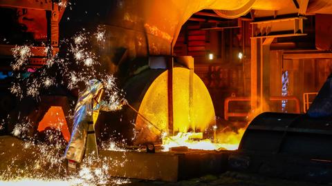 Ein Stahlarbeiter im Schutzanzug entnimmt eine 1500 Grad heisse Roheisenprobe beim Abstich am Hochofen.