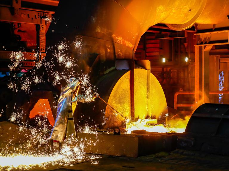 Ein Stahlarbeiter im Schutzanzug entnimmt eine 1500 Grad heisse Roheisenprobe beim Abstich am Hochofen.