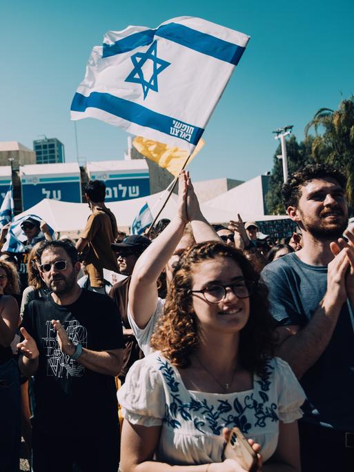 Menschen auf dem Platz der Geiseln feiern die Rückkehr der letzten lebenden Geiseln aus der Gewalt der Hamas. Über ihnen sind Israel-Flaggen zu sehen.