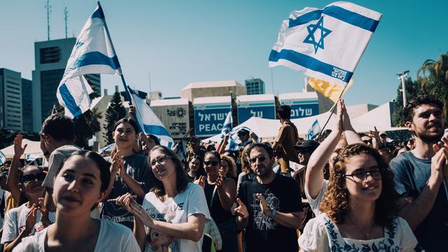 Menschen auf dem Platz der Geiseln feiern die Rückkehr der letzten lebenden Geiseln aus der Gewalt der Hamas. Über ihnen sind Israel-Flaggen zu sehen. Menschen auf dem Platz der Geiseln feiern die Rückkehr der letzten lebenden Geiseln aus der Gewalt der Hamas. Über ihnen sind Israel-Flaggen zu sehen.