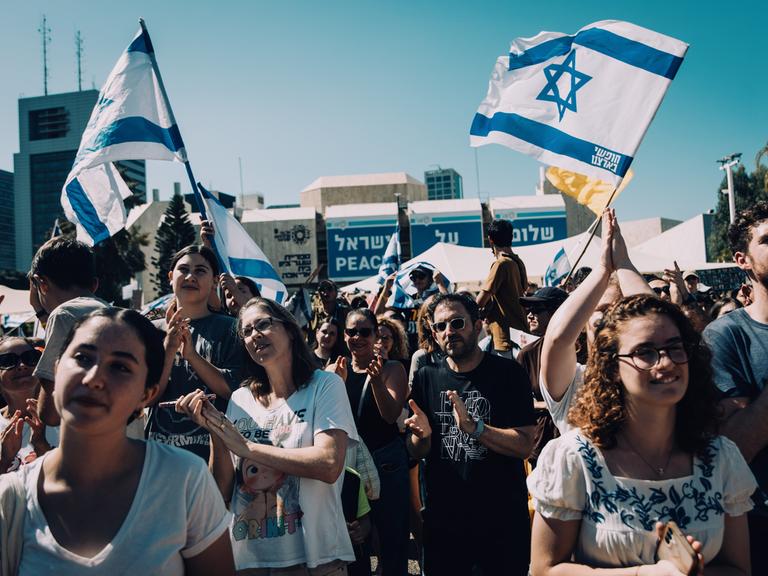 Menschen auf dem Platz der Geiseln feiern die Rückkehr der letzten lebenden Geiseln aus der Gewalt der Hamas. Über ihnen sind Israel-Flaggen zu sehen.