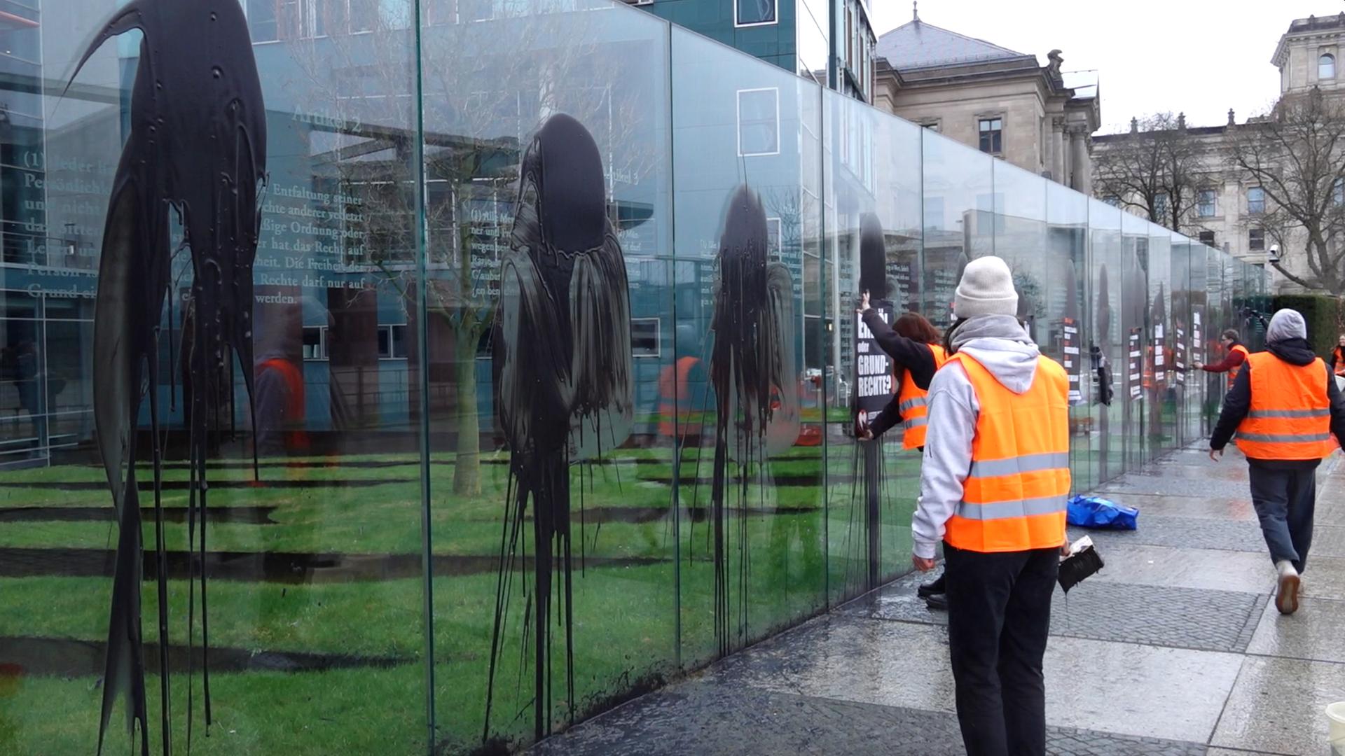 Klimaaktivisten der "Letzten Generation" kippen schwarze Farbe gegen die Glaswände und kleben Plakate an.
