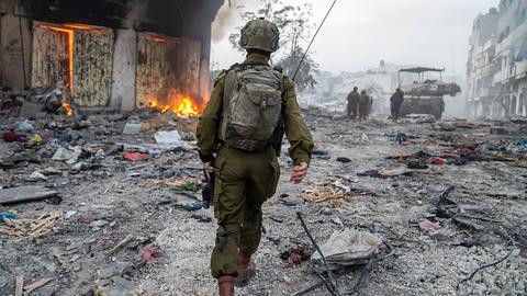 Ein israelischer Soldat geht über einen mit Trümmern übersäten Platz neben einem brennenden Haus.