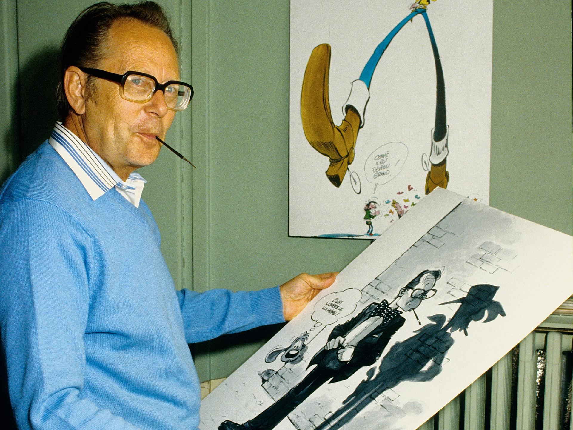 Der Zeichner Maurice De Bevere (Morris), Erfinder von Lucky Luke, steht mit einer großen Skizze in der Hand und einem Zeichenstift im Mund in seinem Büro (1984).