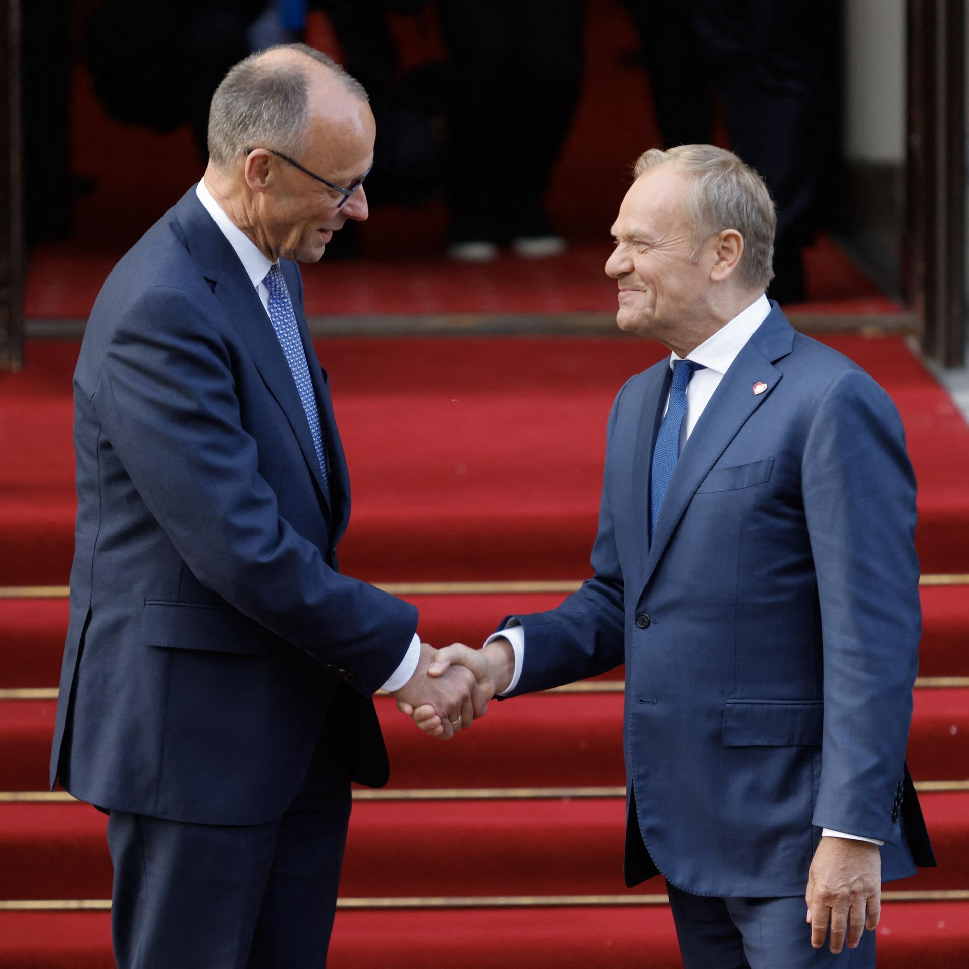 Der polnische Ministerpräsident Donald Tusk (rechts) begrüßt auf einem roten Teppich per Handschlag den neu gewählten deutschen Bundeskanzler Friedrich Merz am 7. Mai 2025 vor dem Regierungsgebäude in Warschau. 