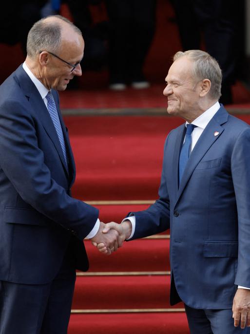 Der polnische Ministerpräsident Donald Tusk (rechts) begrüßt auf einem roten Teppich per Handschlag den neu gewählten deutschen Bundeskanzler Friedrich Merz am 7. Mai 2025 vor dem Regierungsgebäude in Warschau. 