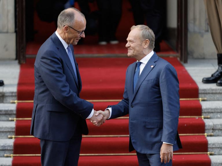 Der polnische Ministerpräsident Donald Tusk (rechts) begrüßt auf einem roten Teppich per Handschlag den neu gewählten deutschen Bundeskanzler Friedrich Merz am 7. Mai 2025 vor dem Regierungsgebäude in Warschau. 