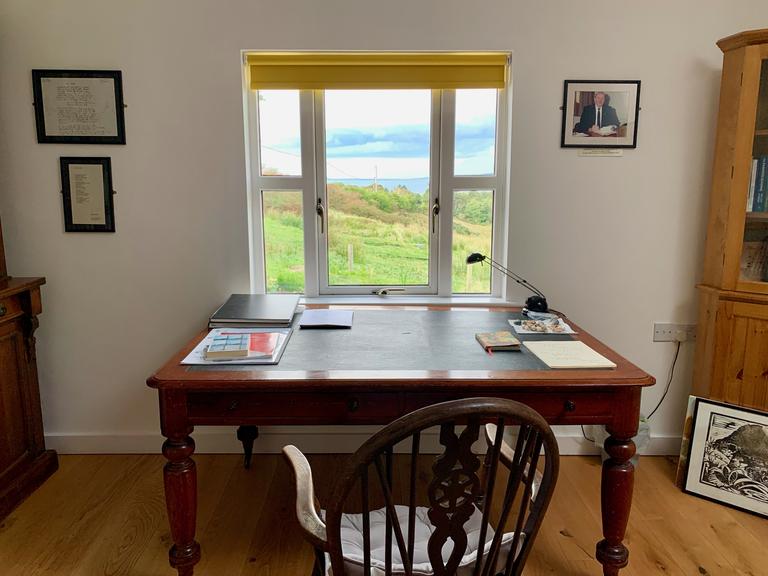 Ein Schreibtisch am Fenster mit Blick auf eine grüne Wiese und das Meer
