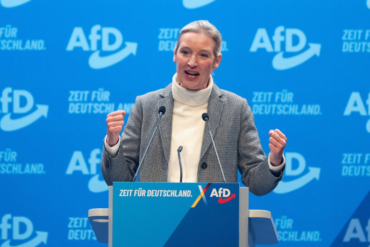 Alice Weidel steht an einem Redner-Pult und hat beide Hände zur Faust geballt. Im Hintergrund eine Wand mit dem AfD-Logo.