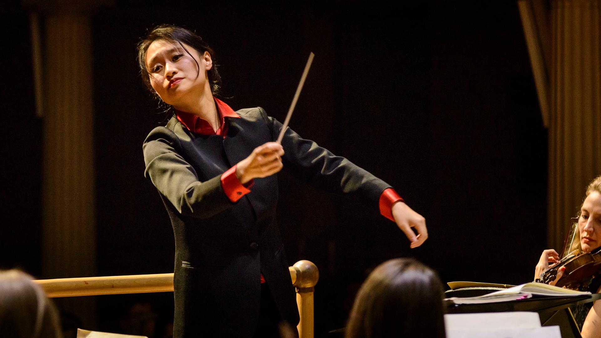 Lu Tianyi dirigiert 2016 in schwarzem Anzug mit roten Armbünden das Met Orchestra.
