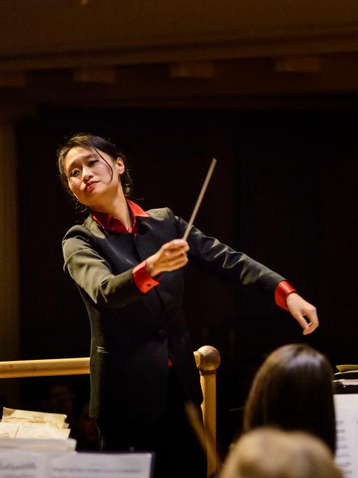 Lu Tianyi dirigiert 2016 in schwarzem Anzug mit roten Armbünden das Met Orchestra.