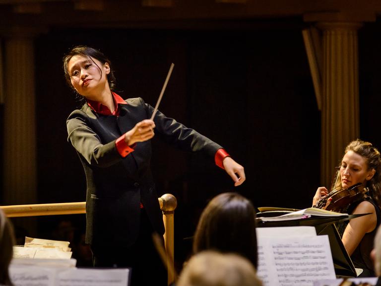 Lu Tianyi dirigiert 2016 in schwarzem Anzug mit roten Armbünden das Met Orchestra.