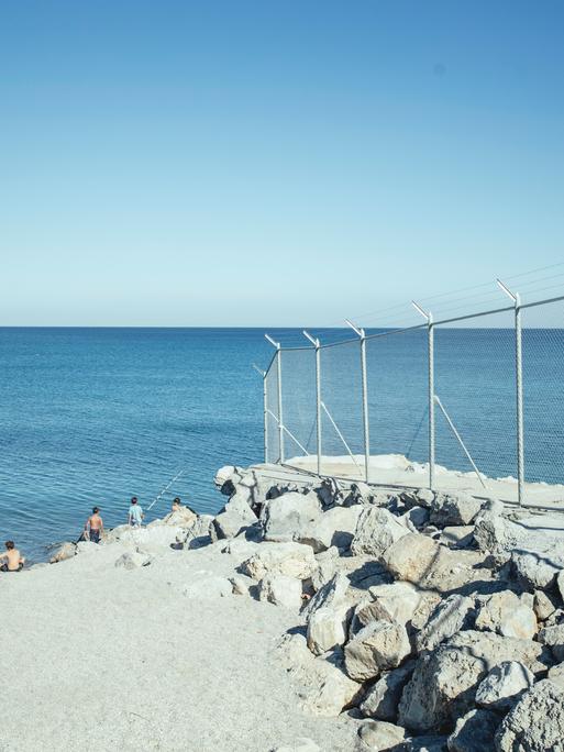 Strand mit Grenzzaun, El Tarajal, Ceuta, Spanien, Europa. Im Hintergrund blaues Meer und blauer Himmel.