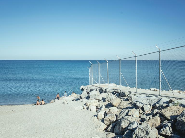Strand mit Grenzzaun, El Tarajal, Ceuta, Spanien, Europa. Im Hintergrund blaues Meer und blauer Himmel.