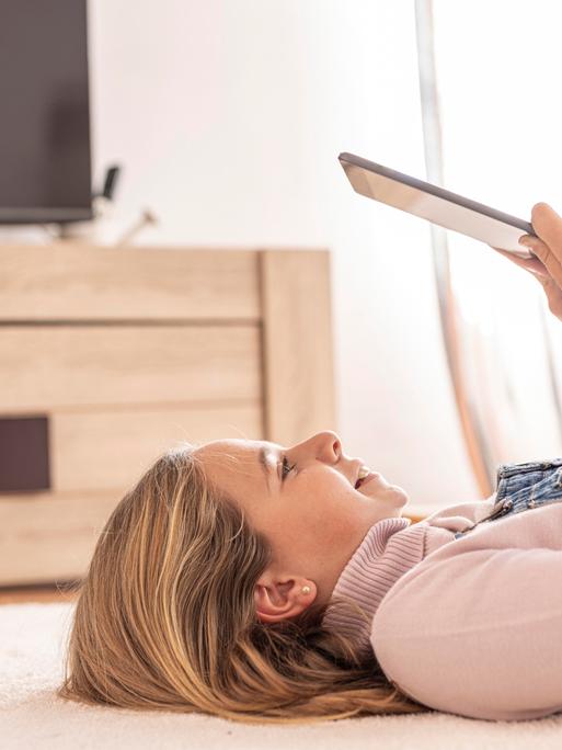 Ein Mädchen liegt auf dem Boden und nutzt ein Tablet
