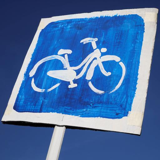 Ein Pappschild mit einem Fahrrad auf blauem Hintergrund vor einem strahlend blauen Himmel.