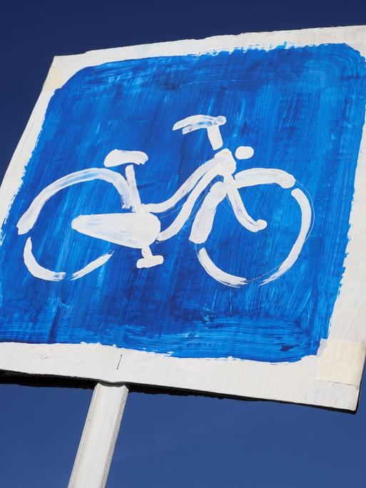 Ein Pappschild mit einem Fahrrad auf blauem Hintergrund vor einem strahlend blauen Himmel.