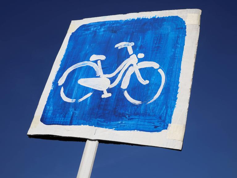 Ein Pappschild mit einem Fahrrad auf blauem Hintergrund vor einem strahlend blauen Himmel.