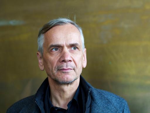 Lutz Seiler blickt ernst ins Off des Bildes. Der Bildhintergrund ist bronzefarben
