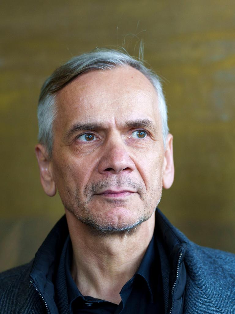 Lutz Seiler blickt ernst ins Off des Bildes. Der Bildhintergrund ist bronzefarben