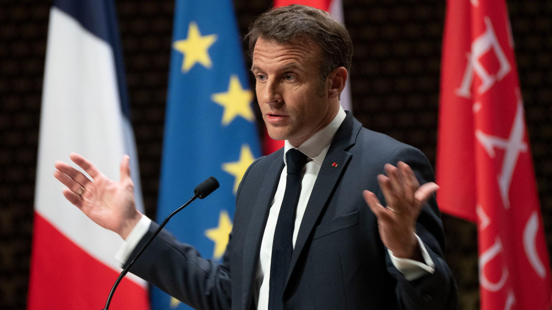 Frankreichs Präsident Macron spricht in einem Theater in Den Haag. Hinter ihm hängen vier verschiedenen Fahnen, darunter die der EU.