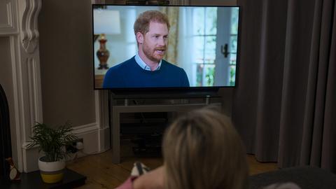 Eine Frau sitzt im Wohnzimmer vor dem Fernseher und schaut das Interview mit dem britischen Prinzen Harry an. 