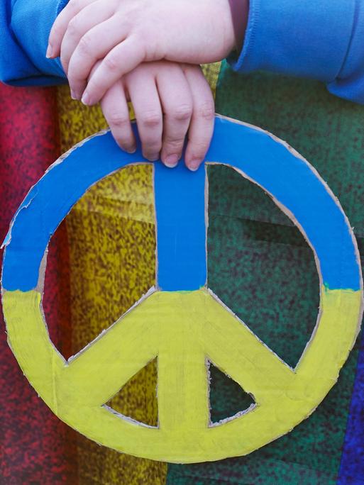 Hände halten ein Friedenszeichen in den Nationalfarben der Ukraine.