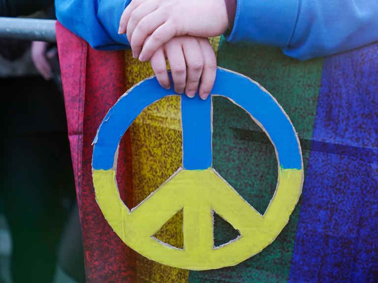 Hände halten ein Friedenszeichen in den Nationalfarben der Ukraine.