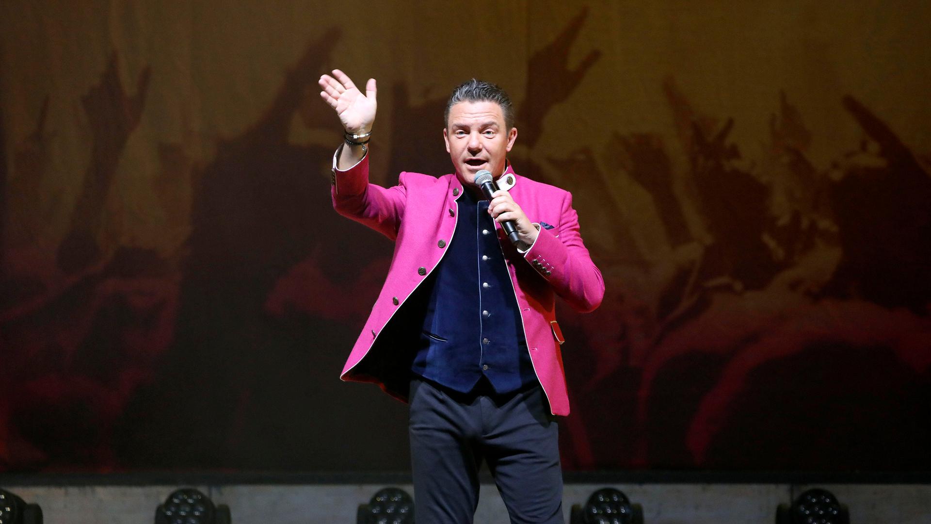 Stefan Mross steht bei der Jubiläums-Tournee von 'Immer wieder sonntags' in der Meistersingerhalle Nürnberg im pinken Trachtenjanker auf der Bühne