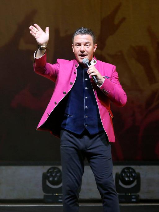 Stefan Mross steht bei der Jubiläums-Tournee von 'Immer wieder sonntags' in der Meistersingerhalle Nürnberg im pinken Trachtenjanker auf der Bühne