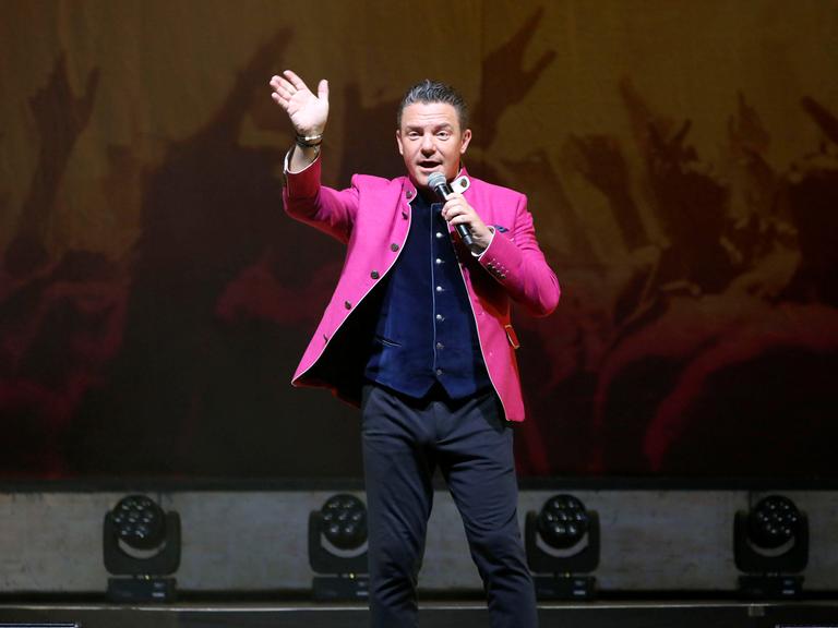 Stefan Mross steht bei der Jubiläums-Tournee von 'Immer wieder sonntags' in der Meistersingerhalle Nürnberg im pinken Trachtenjanker auf der Bühne