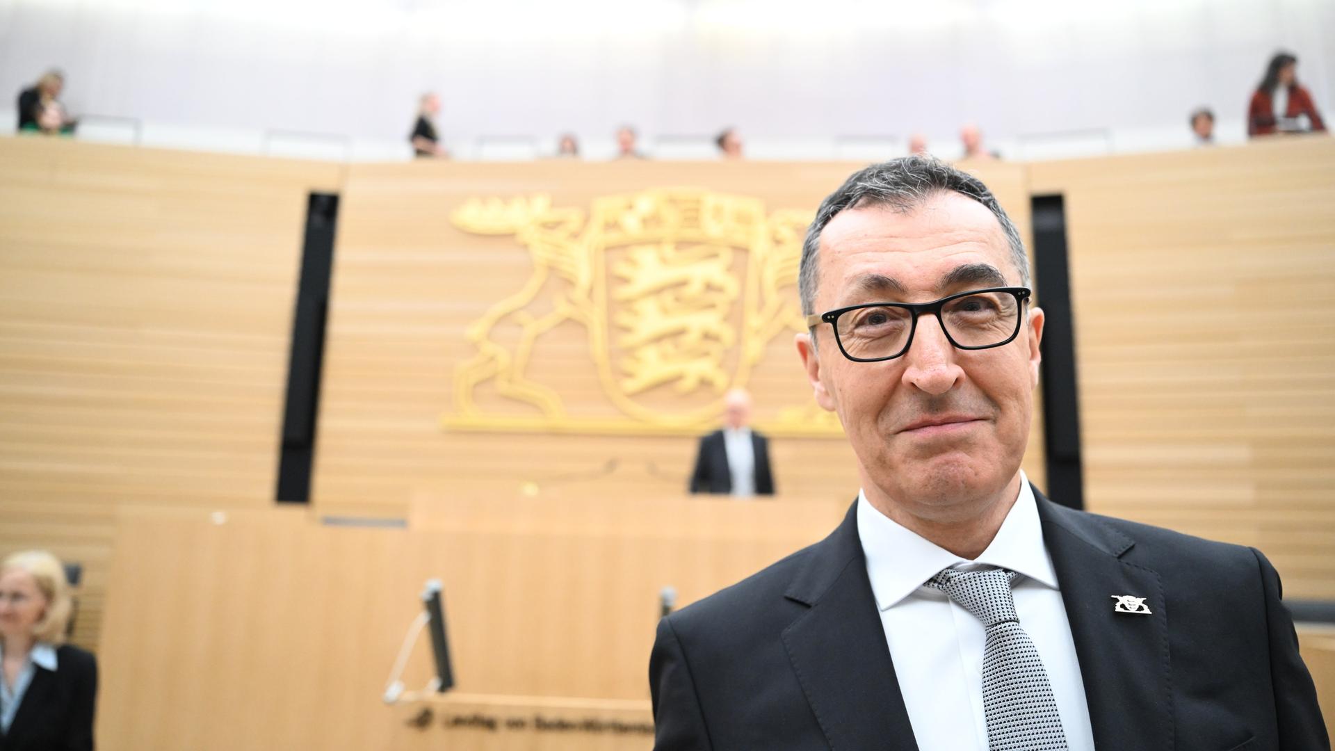Cem Özdemir steht im Landtag in Stuttgart und lächelt in die Kamera.