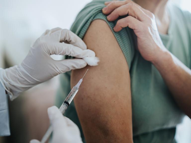 Nahaufnahme eines Armes in den ein Covid-Impfstoff injiziert wird