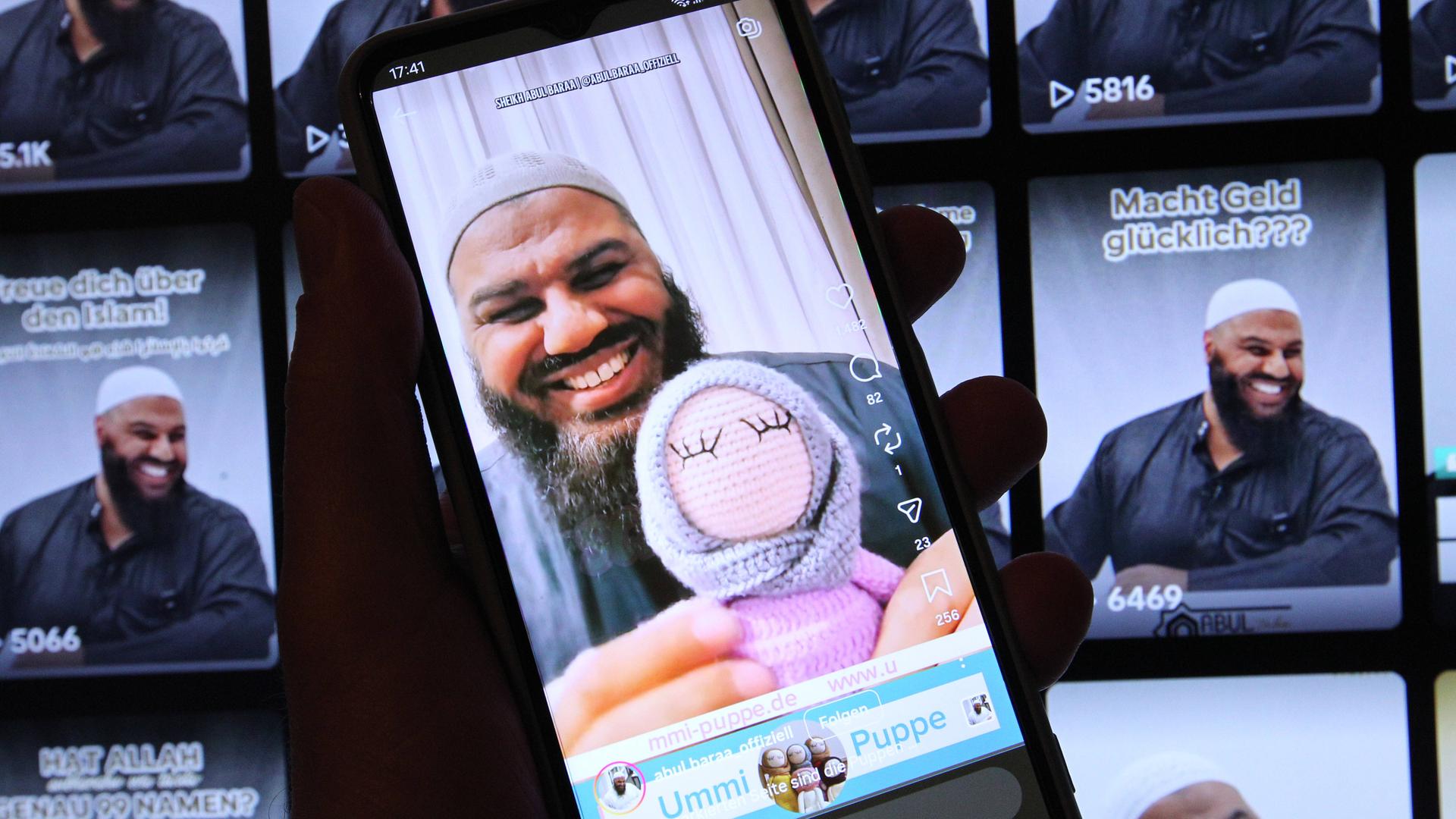 Auf einem Laptop wurde der TikTok-Account von Salafistenprediger Abul Baraa geöffnet. Davor wurde auf einem Smartphone der Instagram-Account des Islam-Influencers geöffnet. Abul Baraa hat eine Stoffpuppe, die ein Kopftuch trägt, in der Hand.