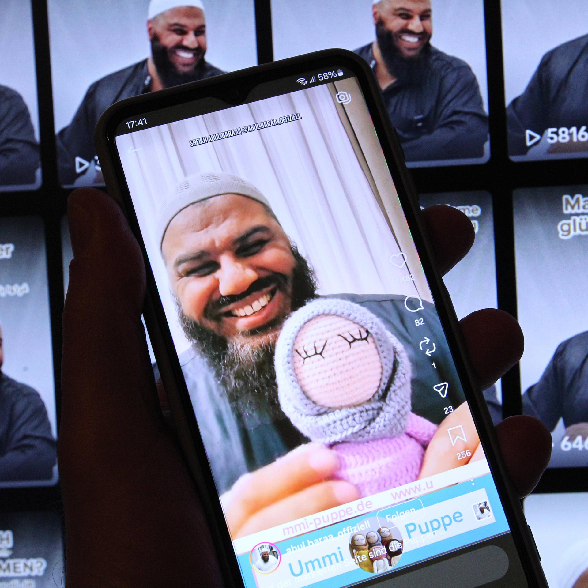 Auf einem Laptop wurde der TikTok-Account von Salafistenprediger Abul Baraa geöffnet. Davor wurde auf einem Smartphone der Instagram-Account des Islam-Influencers geöffnet. Abul Baraa hat eine Stoffpuppe, die ein Kopftuch trägt, in der Hand.