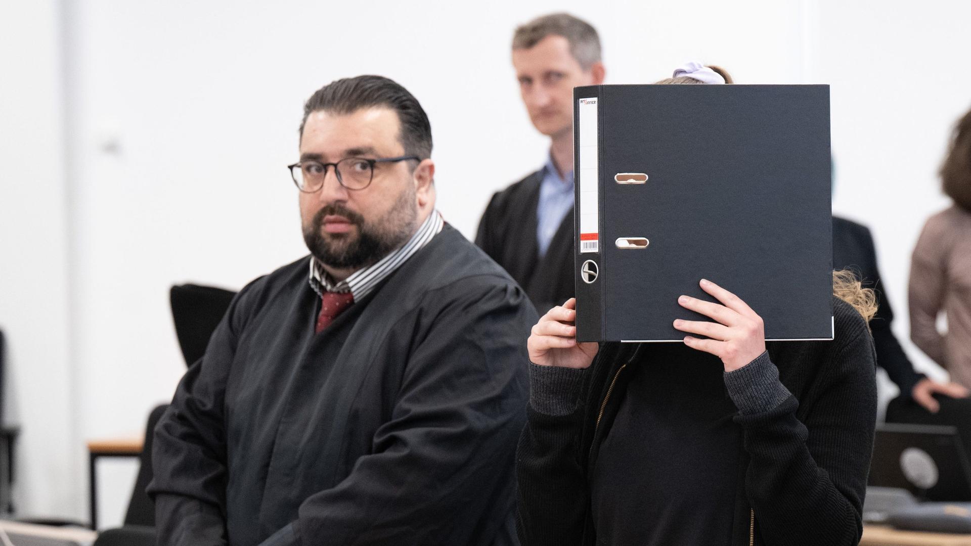 Da Foto zeigt die Angeklagte Lina E. beim Prozess im Oberlandesgericht Dresden. Sie hält im Verhandlungssaal einen Aktenordner vor ihr Gesicht.