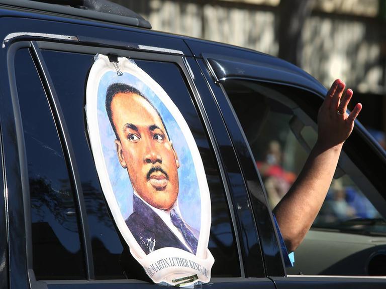 Ein großer Aufkleber mit dem Gesicht von Martin Luther King klebt auf einem Autofenster. Der Beifahrer streckt den Arm aus dem Fenster.
