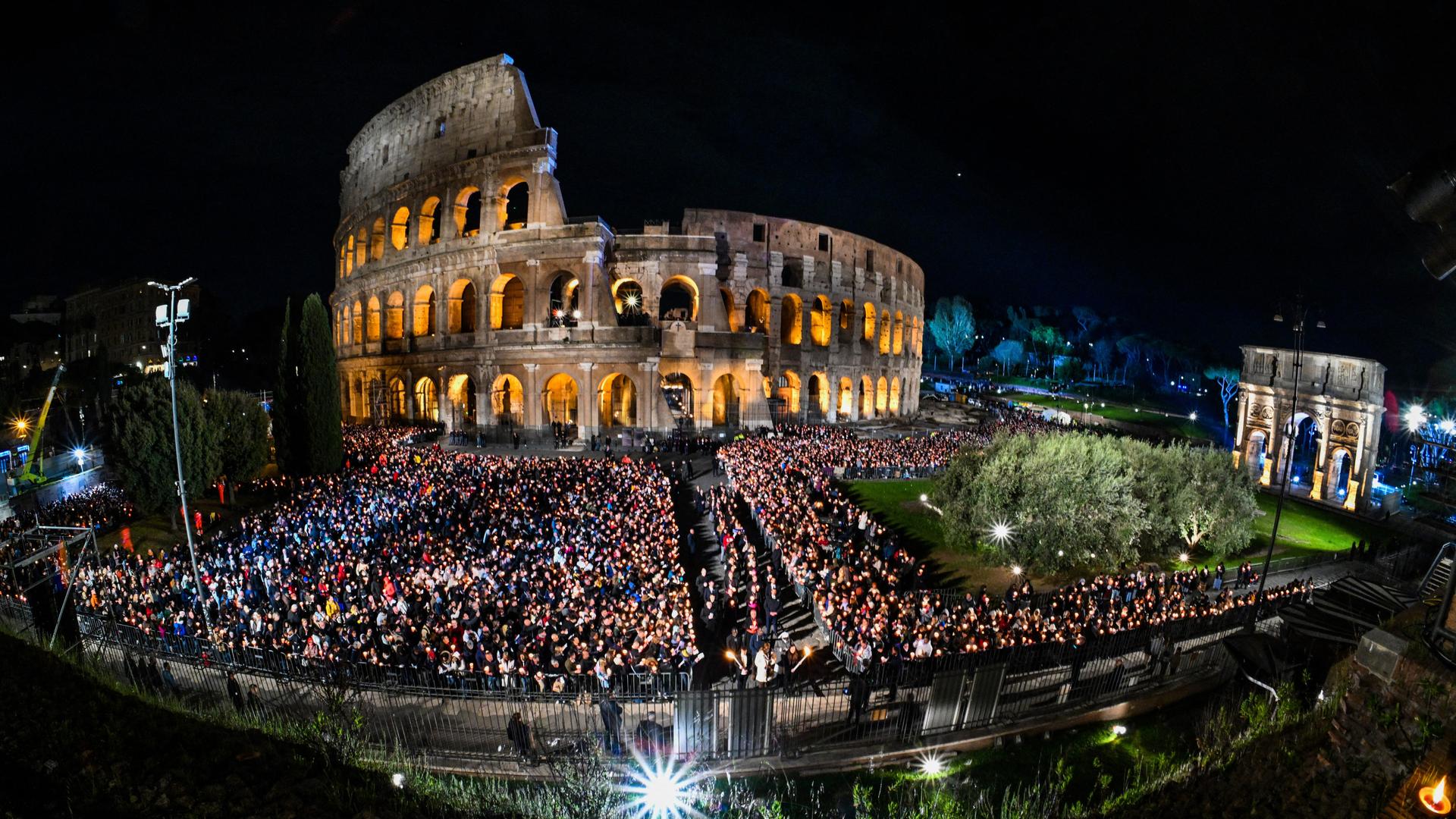 Das Foto zeigt das in der Nacht beleuchtete Kolosseum in Rom und tausende Menschen. (Photo by Andreas SOLARO / AFP)