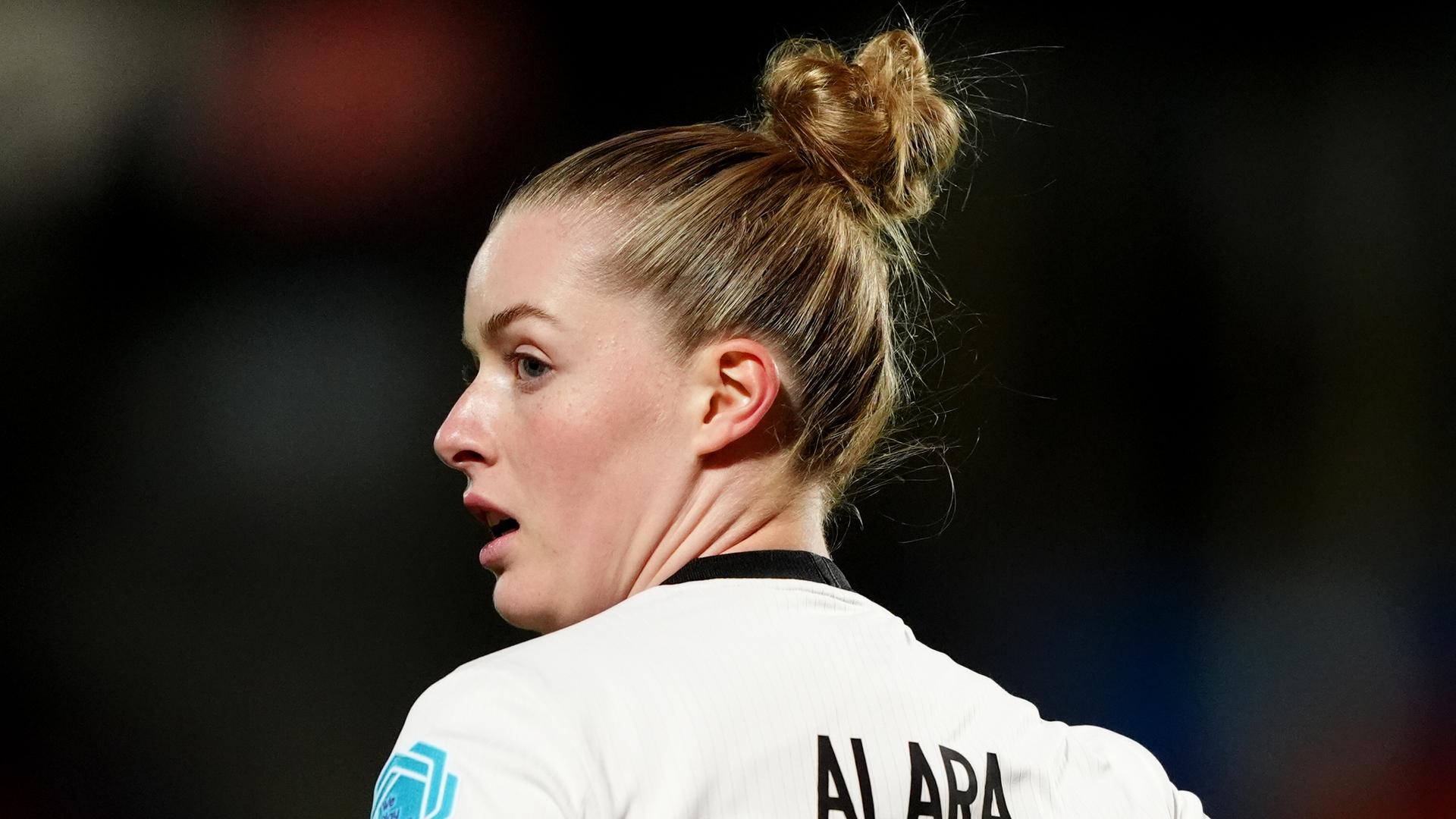 Man sieht sie von hinten; sie dreht sich zur Seite. Sie hat die Haare zum Dutt hochgebunden.