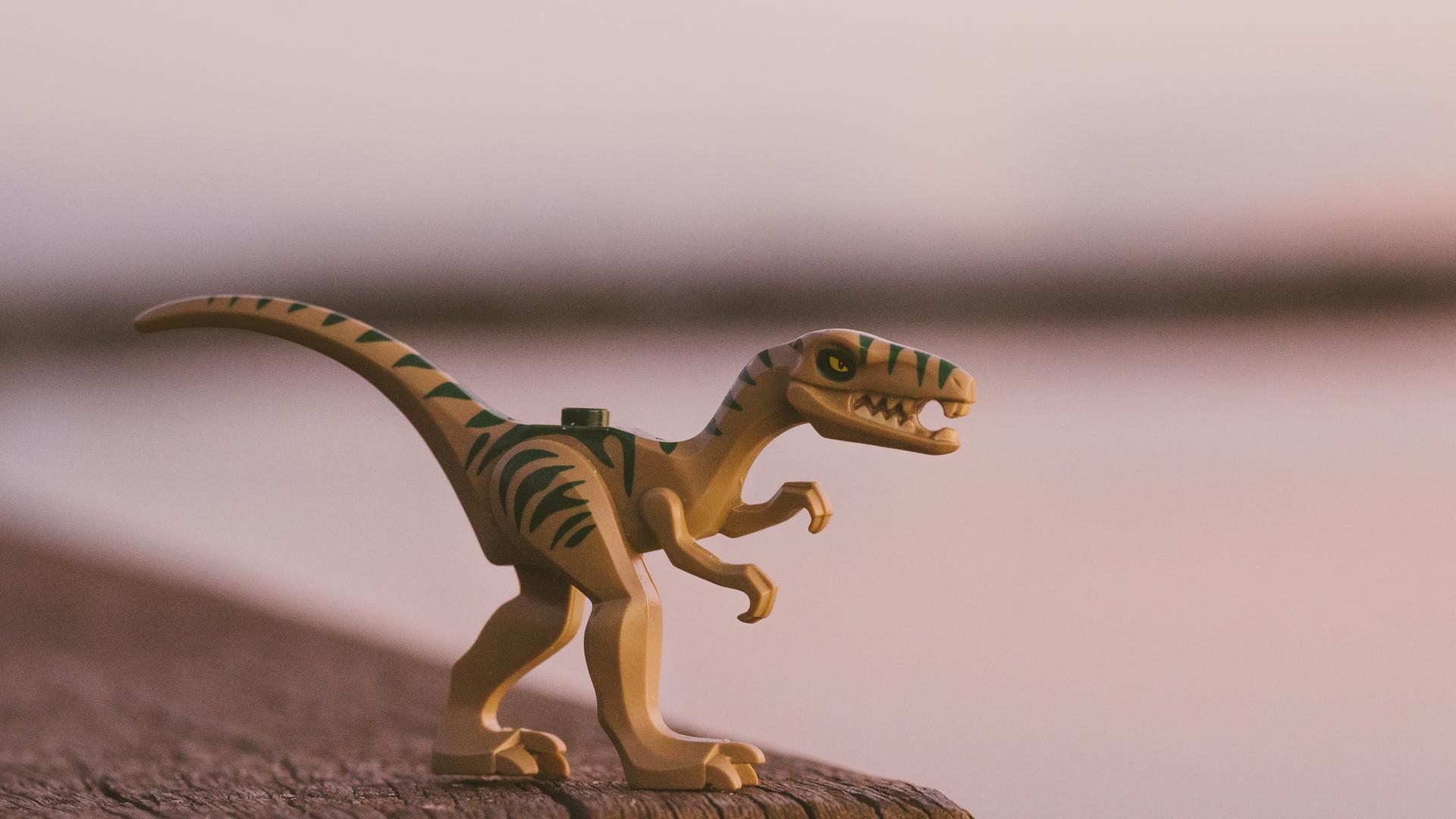 Ein Spielzeugdinosaurier auf hölzernem Untergrund vor unscharfer Kulisse.