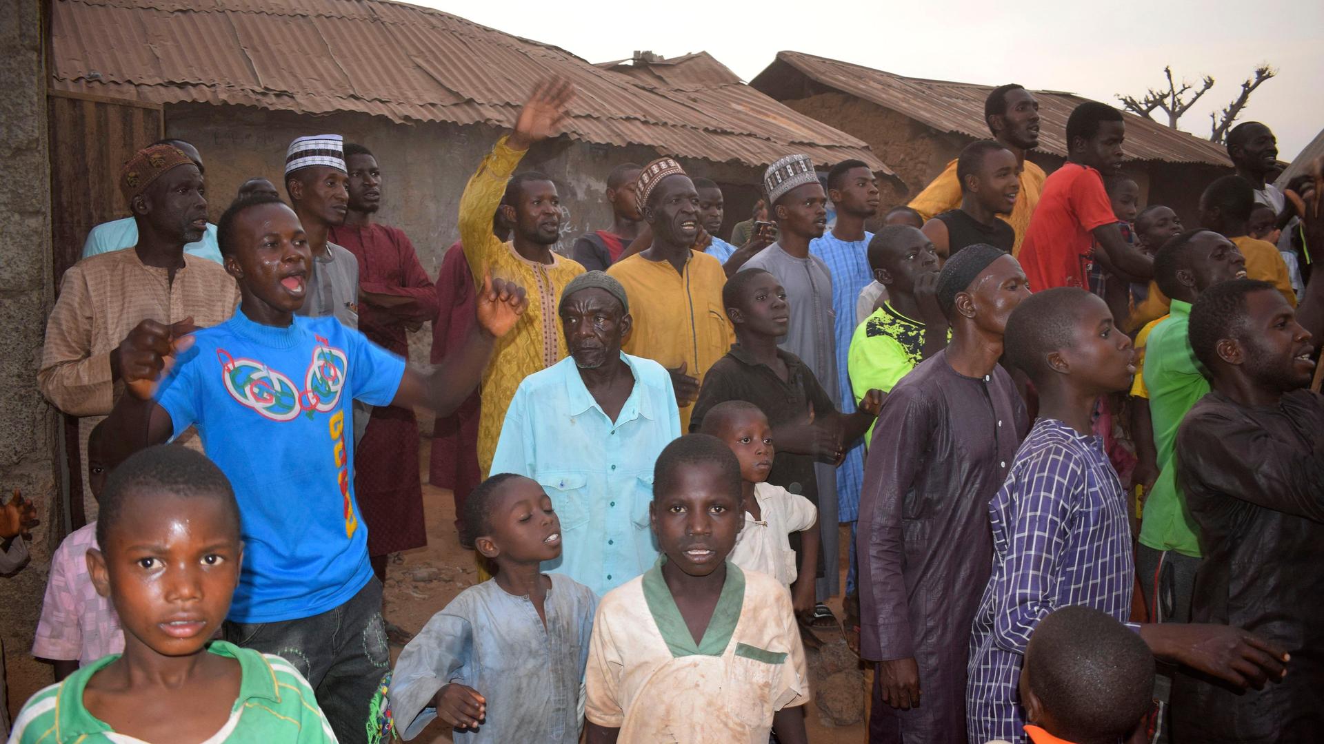 Männer und Kinder rufen etwas in Richtung der nationalen Sicherheitskräfte, die nach der Entführung von Schulkindern in der Region Kaduna eingetroffen sind.